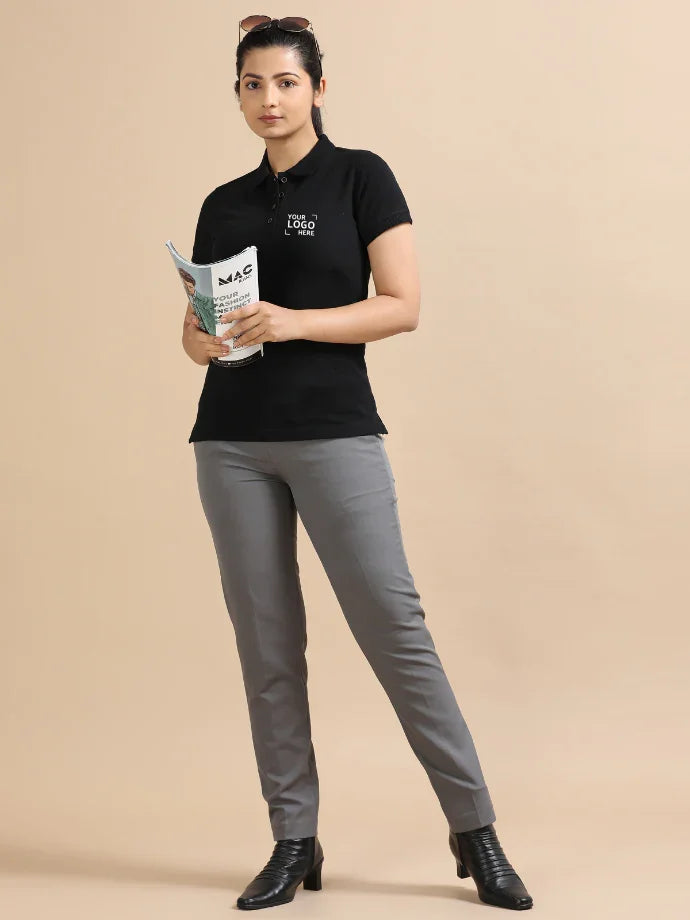 Woman in black custom polo shirt with 'Your Logo Here' text, gray pants, holding magazine, office style